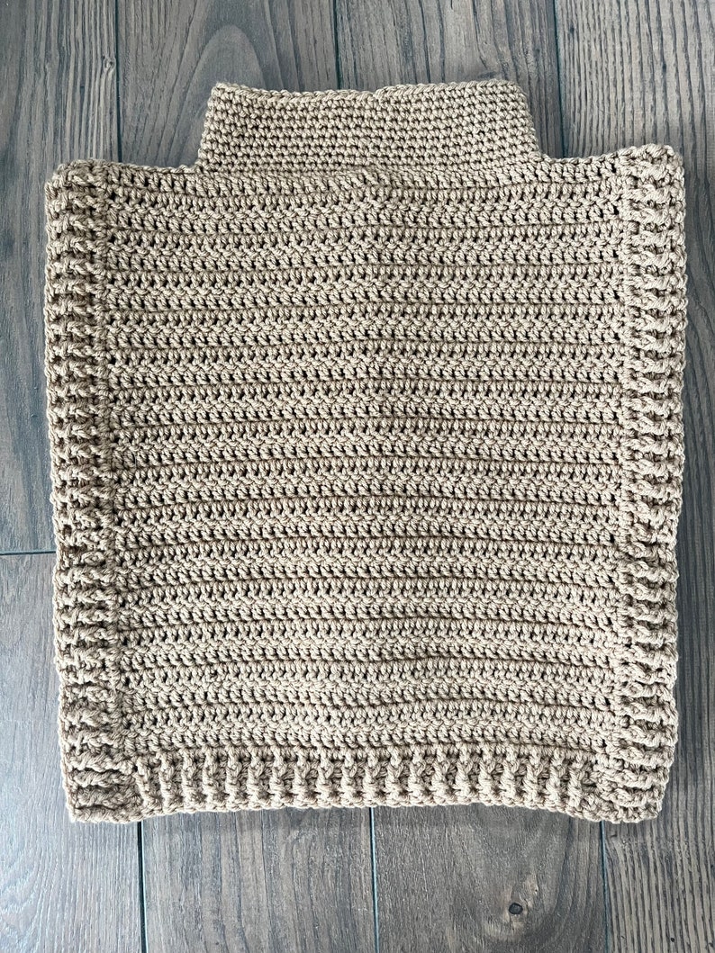 K&ouml;nnte beinhalten: Ein beigefarbener, handgeh&auml;kelter Poncho mit Rollkragen. Der Poncho hat eine rechteckige Form und ein strukturiertes Stichmuster. Die neutrale Farbe und das schlichte Design machen ihn zu einem vielseitigen Kleidungsst&uuml;ck zum &Uuml;berziehen.