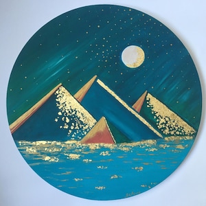May include: A circular painting depicting a night scene with a full moon and a mountain range. The mountains are painted in shades of blue and green, with gold accents. The background is a dark blue sky with gold stars.