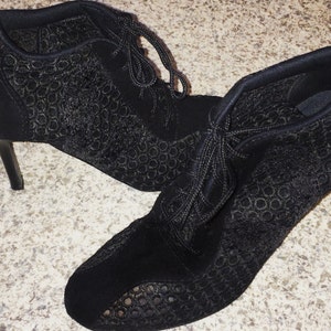 May include: A pair of black heeled ankle boots with lace-up fronts and a delicate patterned design.