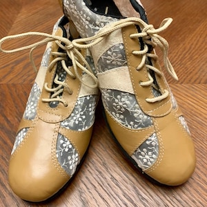 Peut inclure: Une paire de baskets en dentelle beige et blanche avec des accents en cuir beige. Les baskets ont des lacets beiges et un design de chaussure de sport classique. Les panneaux en dentelle présentent un motif floral.