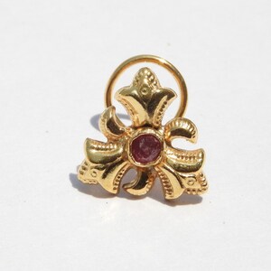May include: A gold nose ring with a red gemstone in the centre and a floral design.