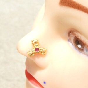 May include: Gold nose ring with a pink stone in the centre. The ring is shaped like a three-pointed star.