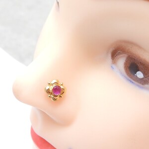 May include: A gold nose ring with a pink gemstone in the centre. The ring is in the shape of a flower with five petals.
