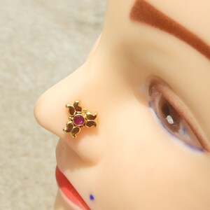 May include: A gold nose ring with a pink gemstone in the centre. The ring is shaped like a flower with three petals.