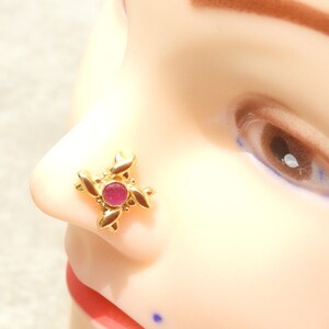 May include: A gold nose ring with a pink stone in the centre and a floral design.