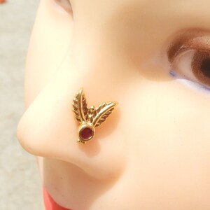 May include: Gold nose ring with a red gemstone and leaf design.