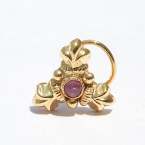 May include: Gold nose ring with a pink gemstone and intricate floral design.