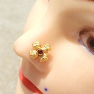 May include: Gold nose ring with a red gemstone in the centre and four flower-shaped accents.