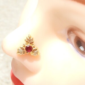 May include: Gold nose ring with a red gemstone and a leaf design.