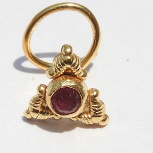 May include: Gold nose ring with a red gemstone and a decorative design.