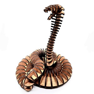 May include: A wooden snake sculpture made of interlocking pieces. The snake is coiled in a circle with its head raised. The sculpture is made of natural wood with a brown finish.