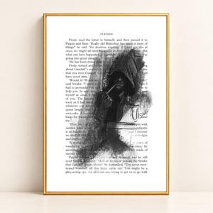 May include: A framed art print featuring a black and white charcoal-style illustration of a hooded figure smoking a pipe, overlaid on a page of printed book text titled Strider. The artwork is encased in a thin, metallic gold-colored frame.