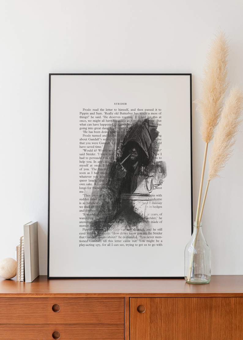 May include: A framed art print featuring a black and white illustration of a hooded figure smoking a pipe, overlaid on a page of printed text titled STRIDER. The artwork is displayed in a thin black frame with a white matting border.