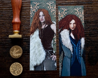 May include: Two bookmarks featuring illustrations of a woman with long red hair. The bookmarks have a green background with gold accents. The woman on the left is wearing a white fur coat and a black tank top. The woman on the right is wearing a blue coat with a white fur collar.