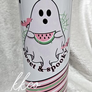 May include: A white tumbler with a black dripped design at the top. The tumbler features a cartoon ghost holding a watermelon slice, with the words "sweet & spooky". The bottom has pink and green stripes.