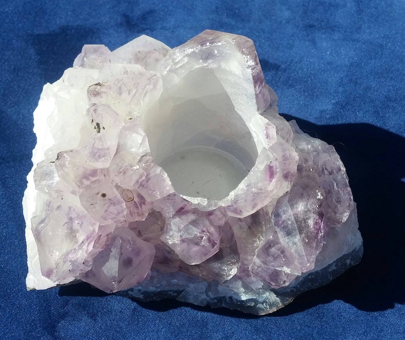 May include: A purple amethyst crystal candle holder with a natural, rough texture. The holder has a hollow center for a candle.