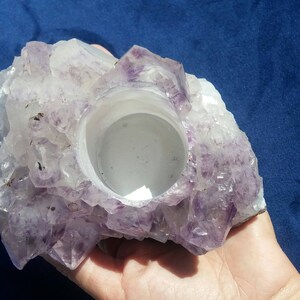 May include: A purple amethyst crystal candle holder with a smooth, white interior. The holder is shaped like a cluster of crystals and has a natural, rough exterior.