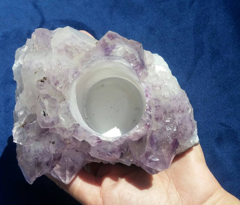 May include: A purple amethyst crystal candle holder with a smooth, white interior. The holder is shaped like a cluster of crystals and has a natural, rough exterior.