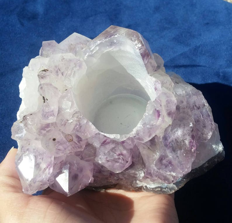 May include: A purple amethyst crystal candle holder with a smooth, white interior. The holder is made of natural amethyst crystals and has a rough, textured exterior.