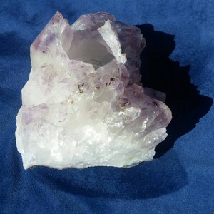 May include: A large, clear quartz crystal with purple amethyst inclusions. The crystal has a natural, rough texture and a hollow center.