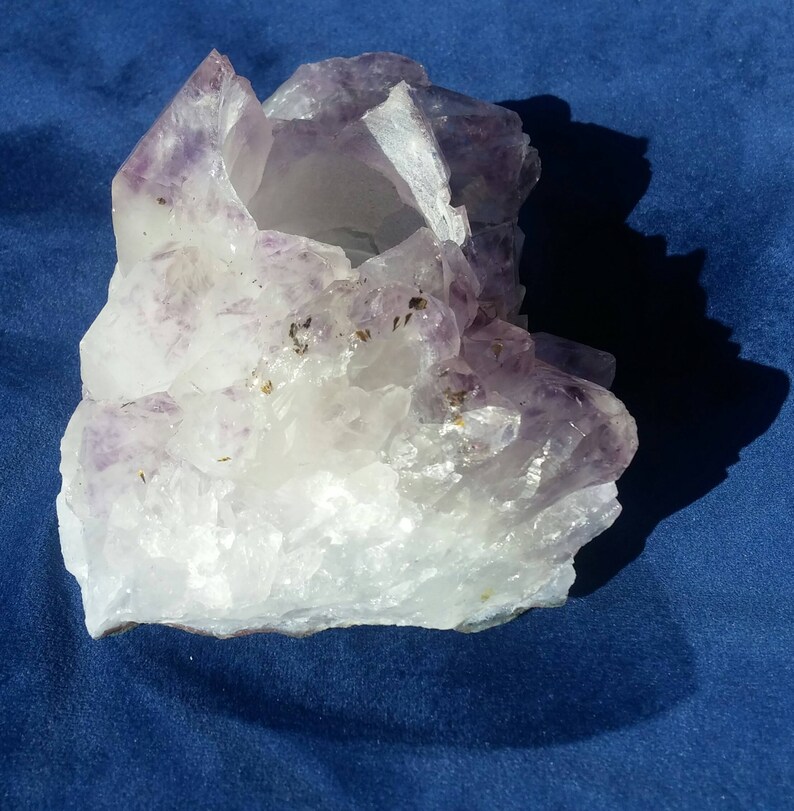 May include: A large, clear quartz crystal with purple amethyst inclusions. The crystal has a natural, rough texture and a hollow center.