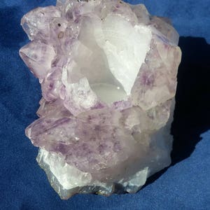 May include: A large amethyst crystal cluster with a hollow center, perfect for displaying or using as a candle holder. The crystal is a deep purple color with a white, translucent center.