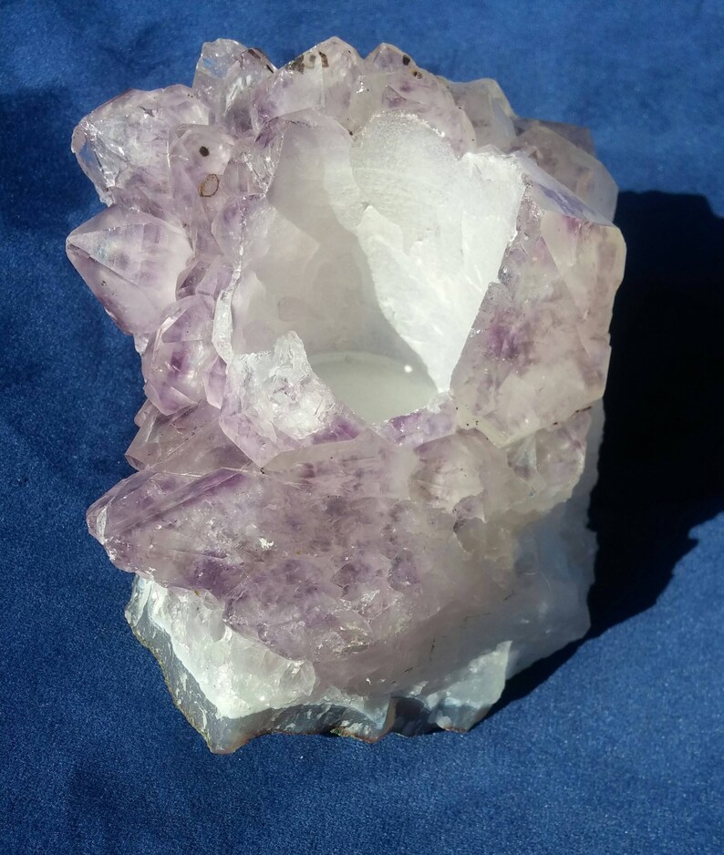 May include: A large amethyst crystal cluster with a hollow center, perfect for displaying or using as a candle holder. The crystal is a deep purple color with a white, translucent center.
