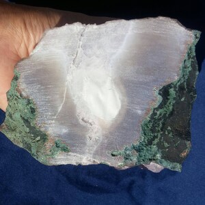 May include: A large, white, translucent agate geode with a green and copper colored exterior. The geode is cut in half, revealing the interior crystals.