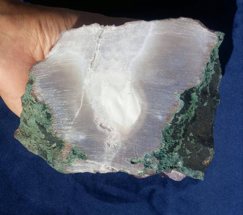 May include: A large, white, translucent agate geode with a green and copper colored exterior. The geode is cut in half, revealing the interior crystals.