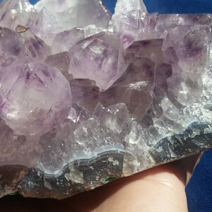 May include: A large amethyst geode with a cluster of purple crystals on a natural base. The geode has a dark grey band around the edge.