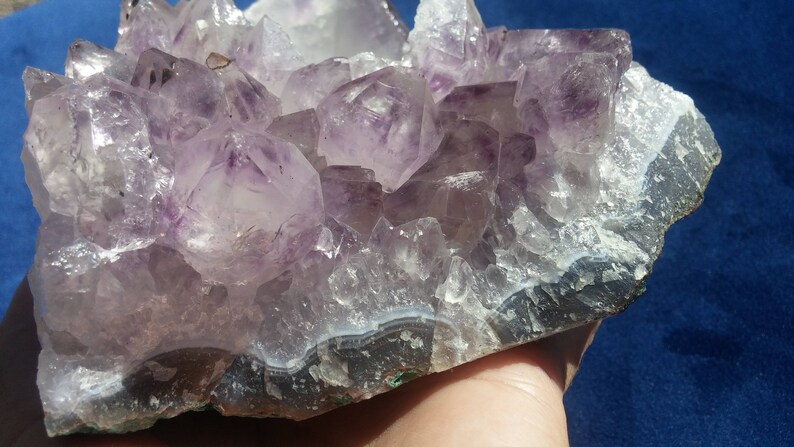 May include: A large amethyst geode with a cluster of purple crystals on a natural base. The geode has a dark grey band around the edge.