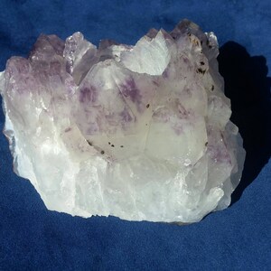 May include: A large, clear quartz crystal cluster with purple amethyst crystals embedded throughout. The cluster has a natural, rough texture and is a beautiful example of a natural crystal formation.
