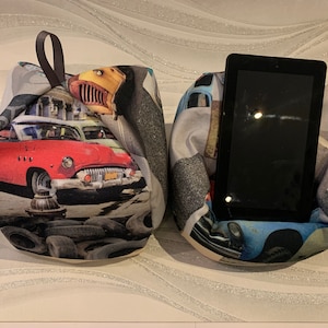 May include: Two beanbag-style tablet holders with a vintage car print. The holder on the left has a red car and the holder on the right has a blue car.