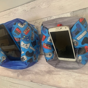 Op de afbeelding: Twee blauwe en grijze beanbag telefoon- en tablet-houders met een gamer-thema. De beanbags zijn bedekt met een stof met een patroon van videogamecontrollers en spelconsoles. Een beanbag houdt een tablet vast en de andere een smartphone.