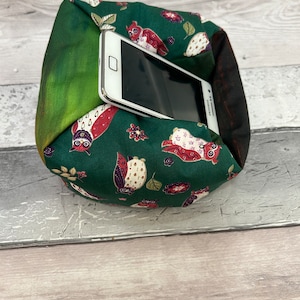 May include: A green fabric phone stand with a white phone inside. The fabric has a pattern of owls and flowers.