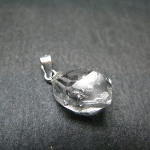 May include: A clear quartz crystal pendant with a silver bail. The crystal is faceted and has a natural, rough appearance.