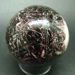 Può includere: Una sfera nera con un motivo a marmo rosso e bianco. La sfera è realizzata in pietra lucidata e ha una superficie liscia.