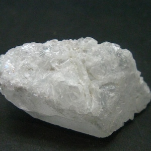 Può includere: Una grande roccia bianca translucida con una superficie ruvida e irregolare. La roccia ha una struttura cristallina e sembra essere composta da più piccoli cristalli.