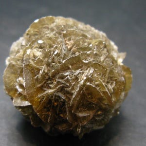 May include: A close-up of a mineral specimen with a spherical shape. The mineral has a layered, crystalline structure and a light brown color with some areas appearing translucent. The surface has a rough, textured appearance.