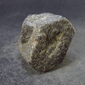 May include: A dark gray, cube-shaped rock with a rough, textured surface.