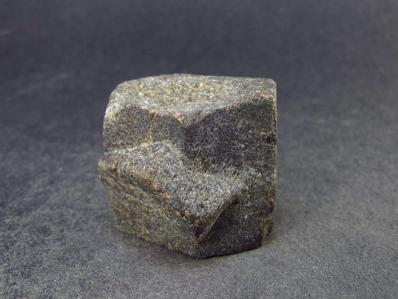 May include: A dark gray, rough, hexagonal shaped rock with a star-shaped pattern on its surface.