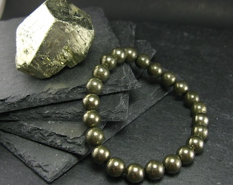 May include: A gold pyrite bracelet with round beads on a black slate background. The bracelet is made of natural pyrite stones.