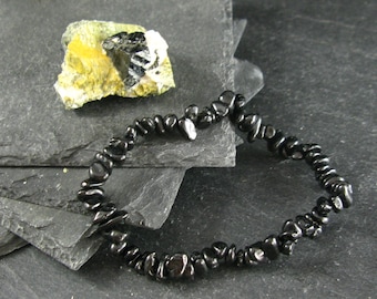 May include: Black gemstone chip bracelet made of small, irregular shaped beads. The bracelet is on a dark grey background.