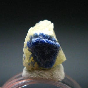 May include: A small, blue and white crystal specimen. The crystal is a light blue color and has a white, opaque base.