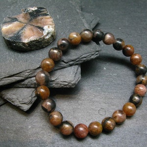 May include: A brown and black gemstone bracelet with round beads. The bracelet is made of natural stones and is approximately 7 inches in length.