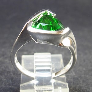 Op de afbeelding: Een zilveren ring met een grote, felgroene edelsteen gezet in een uniek, modern ontwerp.