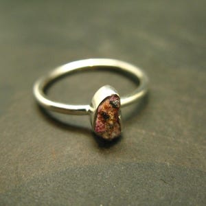 May include: A silver ring with a pink and black stone set in the band.