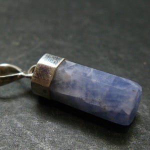 May include: A pendant featuring a faceted, cylindrical light blue stone set in a polished silver-toned metal cap with a matching silver-toned bail at the top. The stone displays a marbled texture with varying shades of blue and white throughout.
