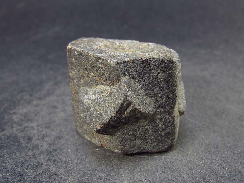 May include: A dark gray, rough, hexagonal shaped rock with a slightly pointed top.