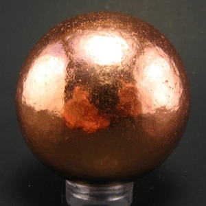May include: A shiny copper sphere with a smooth, reflective surface. The sphere is slightly textured and has a warm, metallic colour.